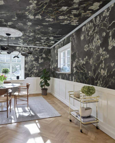 Tapet cu flori de migdal albe pe fundal negru, aplicat pe un perete intr-un living modern.