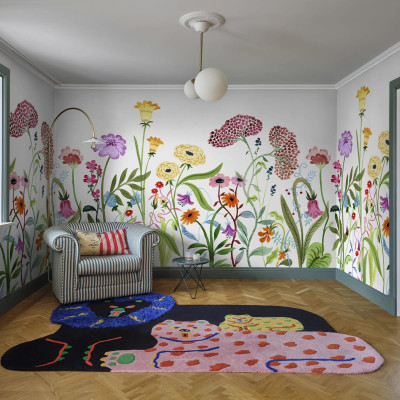 Tapet floral colorat cu flori diverse, aplicat pe un perete din camera de zi, decorata cu o canapea si un covor.