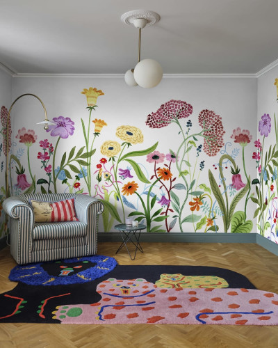 Tapet floral colorat cu flori diverse, aplicat pe un perete din camera de zi, decorata cu o canapea si un covor.