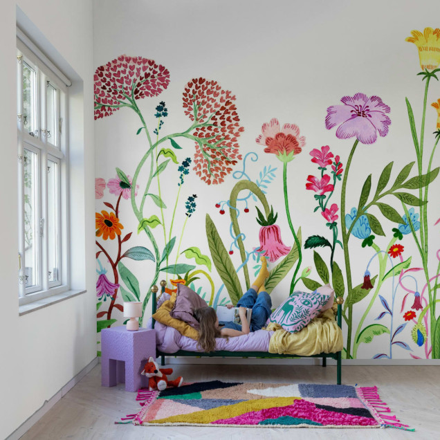 Tapet floral colorat cu flori diverse, aplicat pe un perete din camera de zi, decorata cu o canapea si un covor.