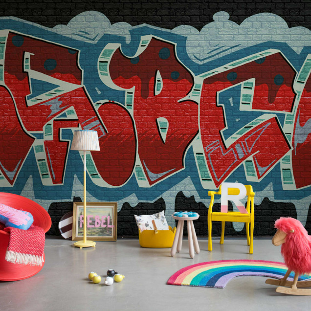 Tapet Rebel Graffiti, Red, cu un design urban in rosu, albastru si verde. Tapetul este pozitionat pe un perete din camera de zi, alaturi de o masa de lucru.