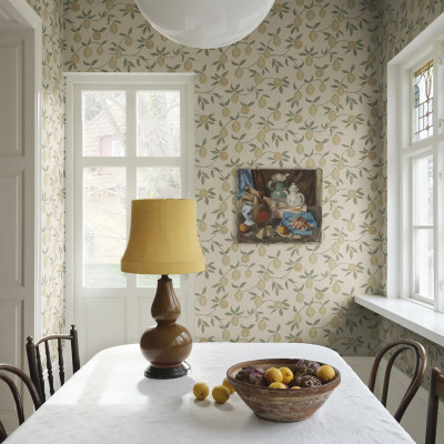 Tapet Limone Yellow cu model de lămâi galbene pe fundal crem, într-o cameră de dining luminoasă cu mobilier clasic și accesorii mediteraneene.