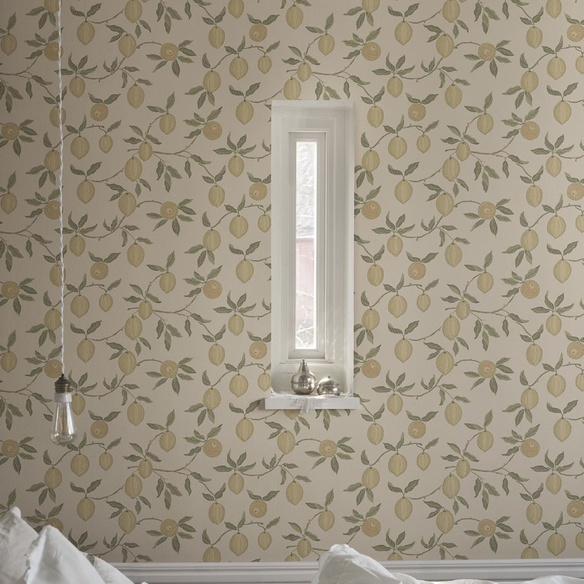 Cameră decorată cu tapet Limone, Blush, prezentând un model repetitiv de lămâi pe fundal roz pal și bej, acoperind pereții și tavanul. Livingul are o canapea maro, masă rotundă și plante verzi, cu o fereastră luminoasă.