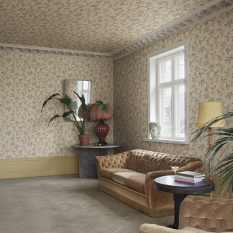 Cameră decorată cu tapet Limone, Blush, prezentând un model repetitiv de lămâi pe fundal roz pal și bej, acoperind pereții și tavanul. Livingul are o canapea maro, masă rotundă și plante verzi, cu o fereastră luminoasă.