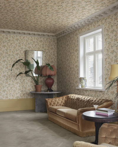Cameră decorată cu tapet Limone, Blush, prezentând un model repetitiv de lămâi pe fundal roz pal și bej, acoperind pereții și tavanul. Livingul are o canapea maro, masă rotundă și plante verzi, cu o fereastră luminoasă.