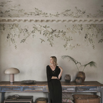Fototapet Luca Sand cu model floral delicat, ramuri cu flori albe și păsări pe un fundal nisipiu, într-o amenajare interioară elegantă și relaxantă.