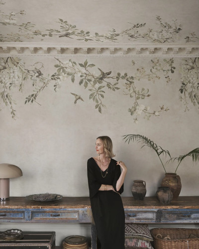 Fototapet Luca Sand cu model floral delicat, ramuri cu flori albe și păsări pe un fundal nisipiu, într-o amenajare interioară elegantă și relaxantă.