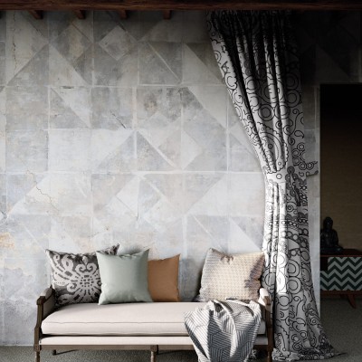 Tapet modern cu model geometric Tintagel, Grey, ilustrat pe un perete din living, lângă un fotoliu gri cu perne decorative.