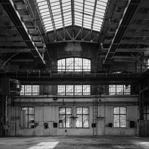 Tapet Industrial Grey, cu un design modern, inspirat de spațiile industriale. Acesta prezintă o imagine a unui hală cu o structură metalică și ferestre mari, în nuanțe de gri.