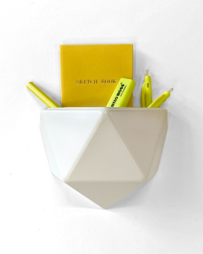 Ghiveci din plastic alb, cu design geometric, atașat pe un perete alb, conținând un carnet galben și markere galbene.