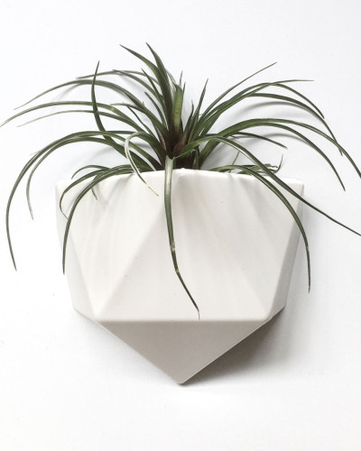 Ghiveci din plastic alb, cu design geometric, atașat pe un perete alb, conținând un carnet galben și markere galbene.