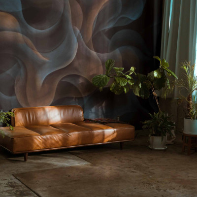 Imagine cu tapet lavabil My Cave Black, Coordonne, cu un design abstract cu nuanțe de negru și gri, prezentând un canapea din piele maro și plante verzi în ghivece.