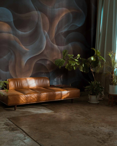 Imagine cu tapet lavabil My Cave Black, Coordonne, cu un design abstract cu nuanțe de negru și gri, prezentând un canapea din piele maro și plante verzi în ghivece.