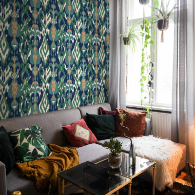 Tapet lavabil Uzbek Green cu model tradițional inspirat din motivele uzbece, aplicat pe peretele unui living, lângă o canapea, cu un covor floral și plante suspendate de la fereastră
