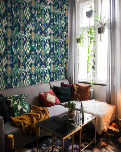 Tapet lavabil Uzbek Green cu model tradițional inspirat din motivele uzbece, aplicat pe peretele unui living, lângă o canapea, cu un covor floral și plante suspendate de la fereastră