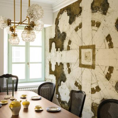 Tapet cu design clasic inspirat de arhitectura florentină,  aflat pe un perete în living, alături de o masă de dining, scaune și un candelabru cu cristale.