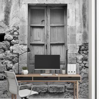 Fototapet alb-negru personalizat Noto Palace Splendor, ilustrând un perete vechi de piatră cu o fereastră de lemn antică, într-un birou modern cu un birou din lemn și un scaun alb.
