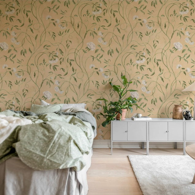 Tapet cu un model floral de bujori în nuanțe de caise și frunze verzi pe un fundal deschis, într-un living decorat cu o canapea din piele.
